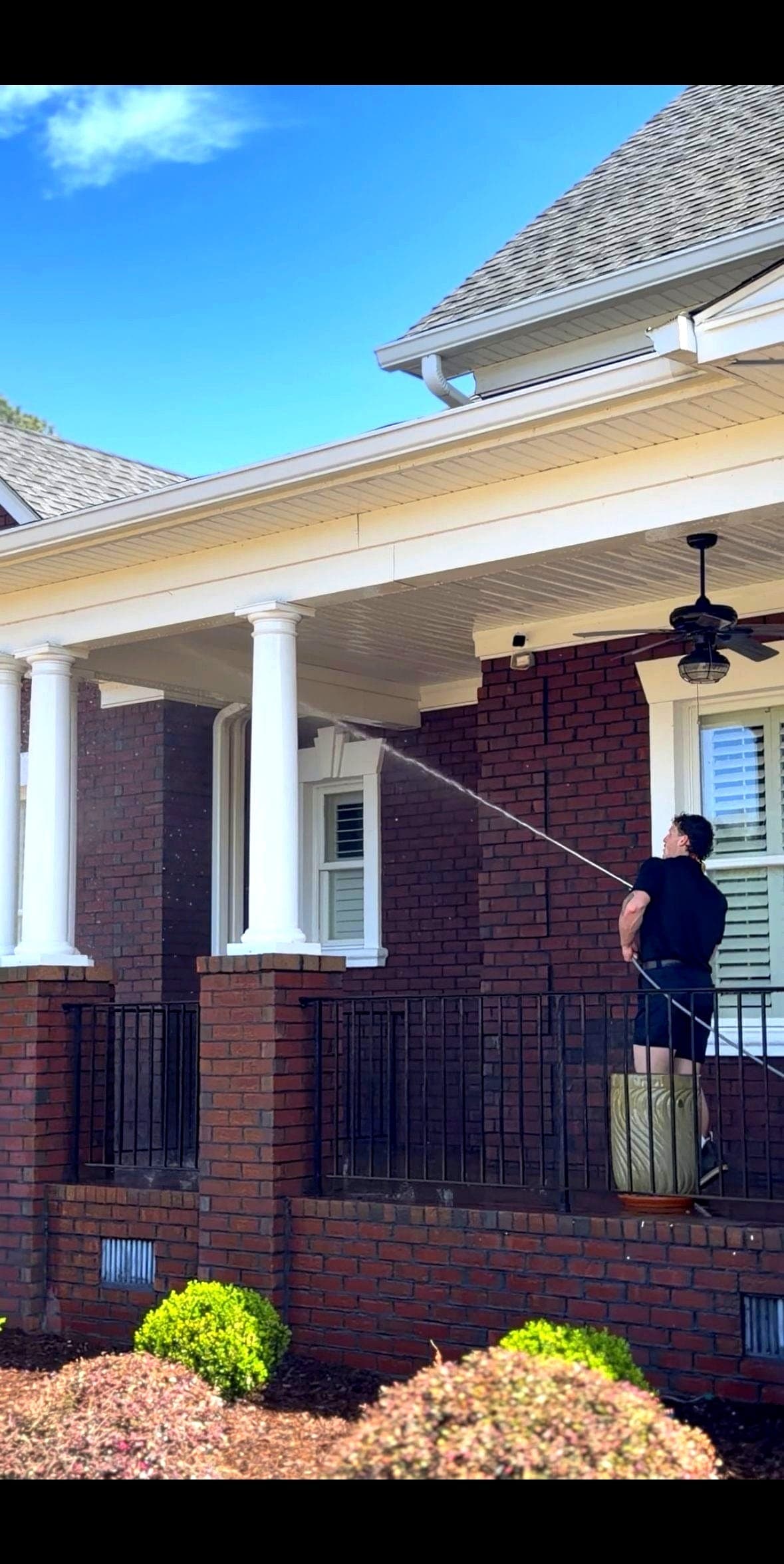 Technician softwashing a brick home exterior with spray wand