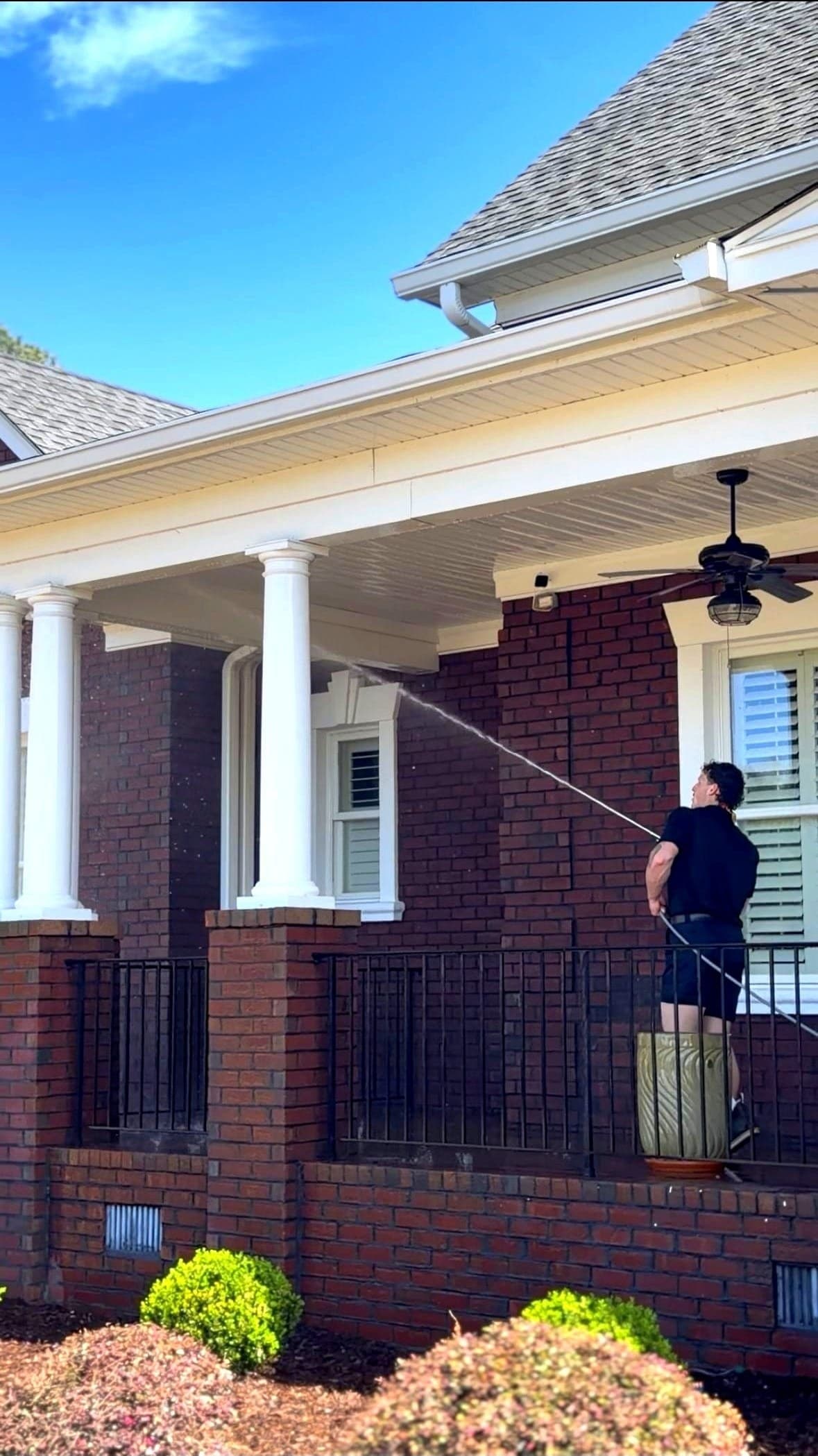 Technician softwashing a brick home exterior in Columbia, SC with a spray wand