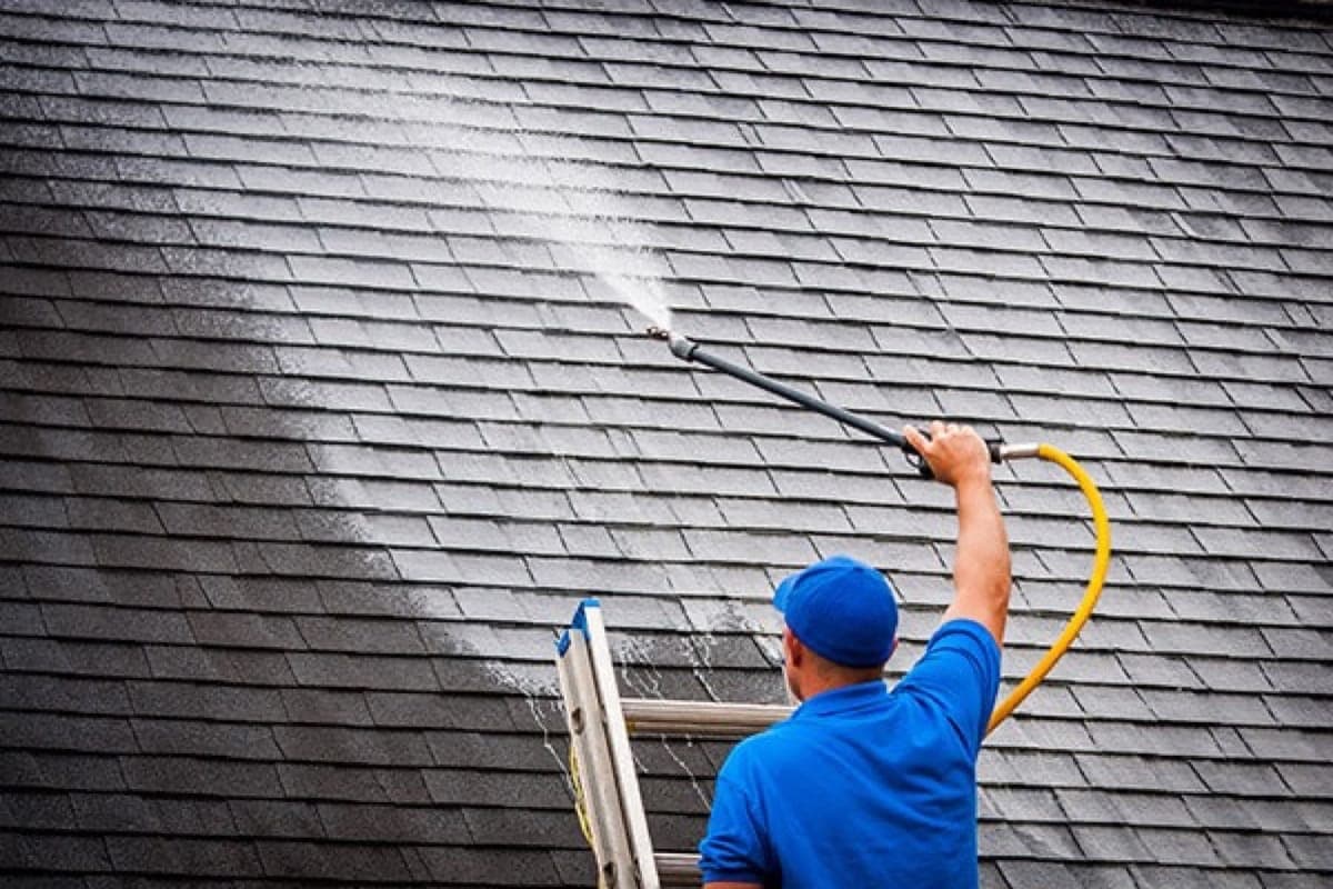 Technician softwashing roof shingles on a Columbia, SC home during professional roof cleaning