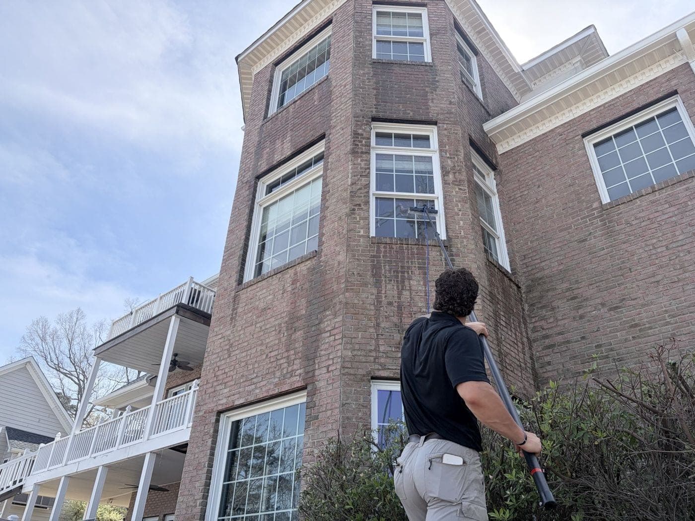 Technician cleaning windows on a brick Lexington, SC home with a water-fed pole