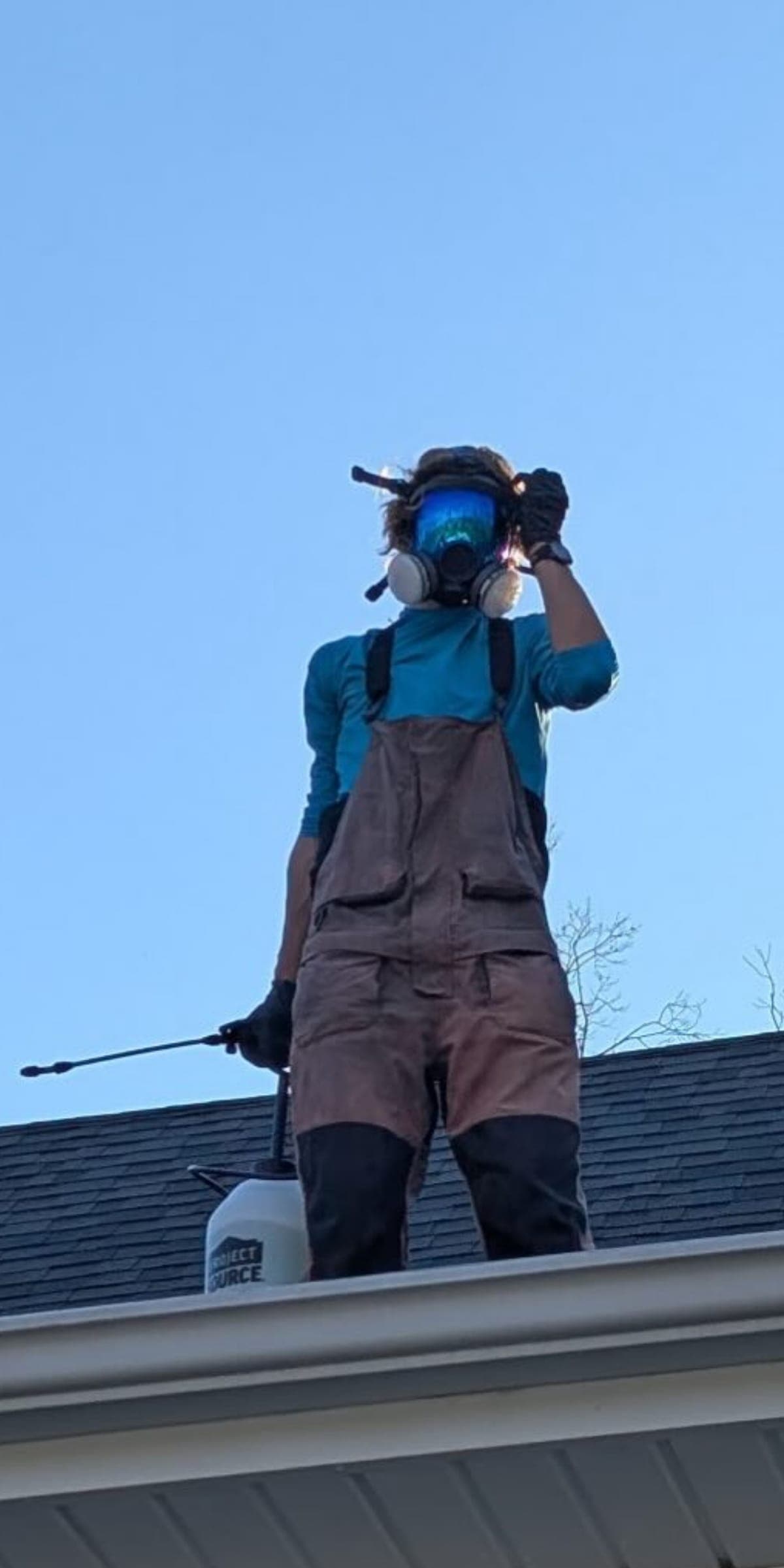Technician with respirator applying roof softwash treatment closeup