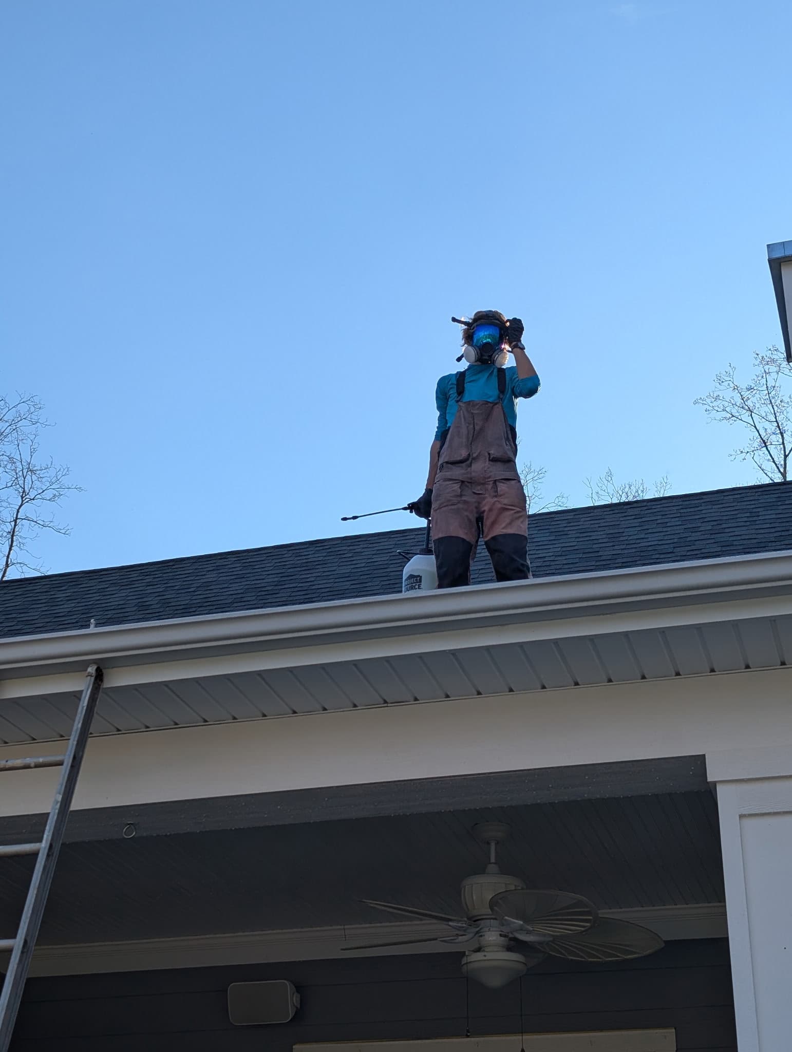 Technician on roof applying softwash treatment with respirator
